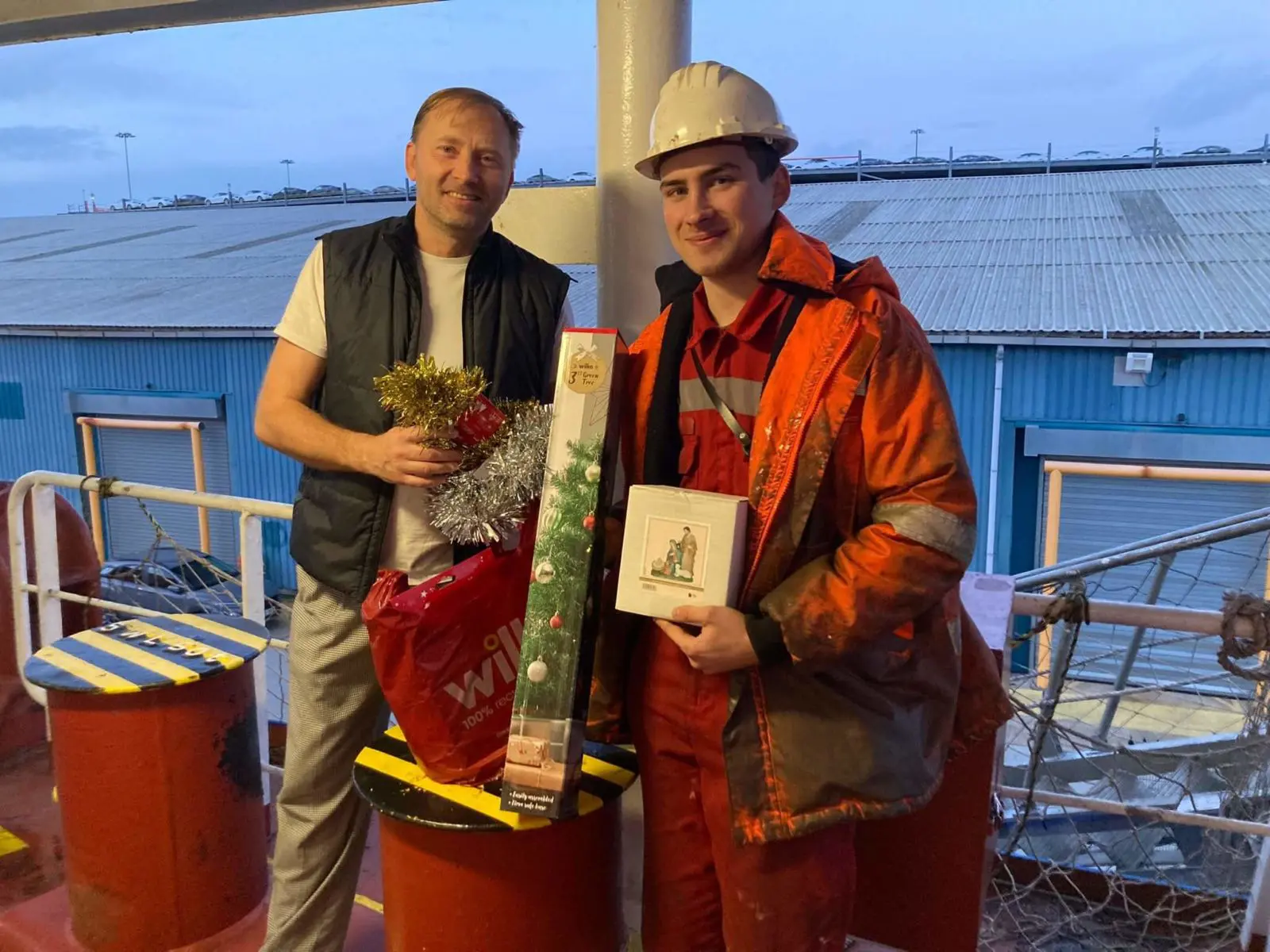 Two people with a Christmas tree. One of the man looks to be a sea worker.